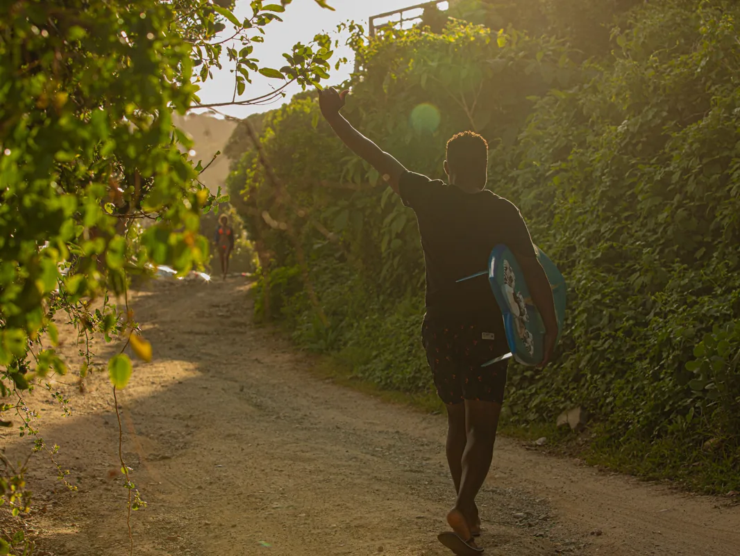A surfer walking up the road to Beach House Wilderness Backpackers with a board under one arm, a hundred metres from the beach